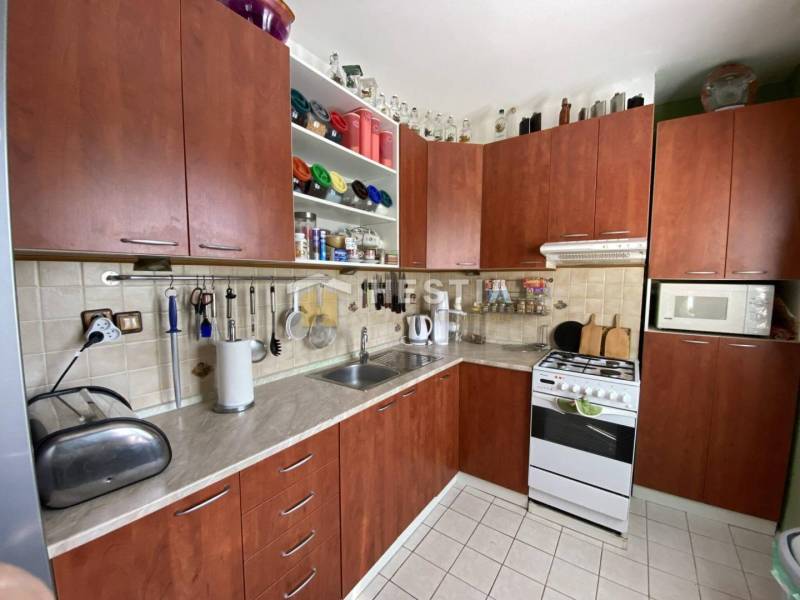 Kuchyně v 2-pokojovém bytě s dřevěnými skříňkami a bílou dlažbou.