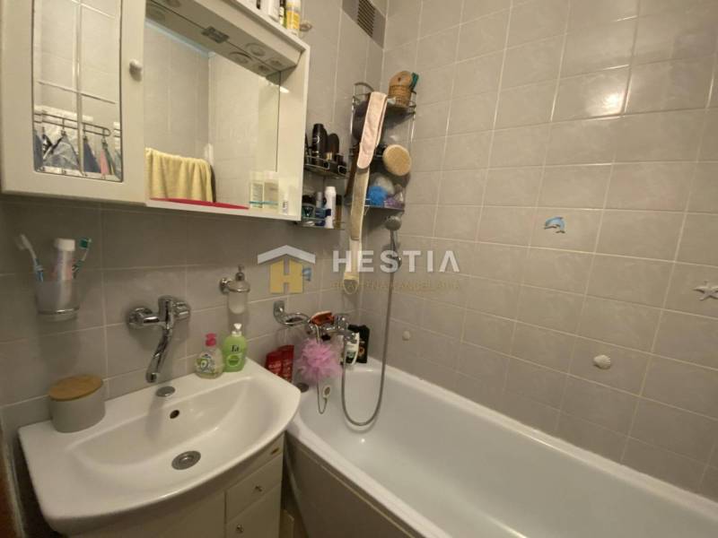 Koupelna se sprchou a umyvadlem ve 2-pokojovém bytě s bílými dlaždicemi.