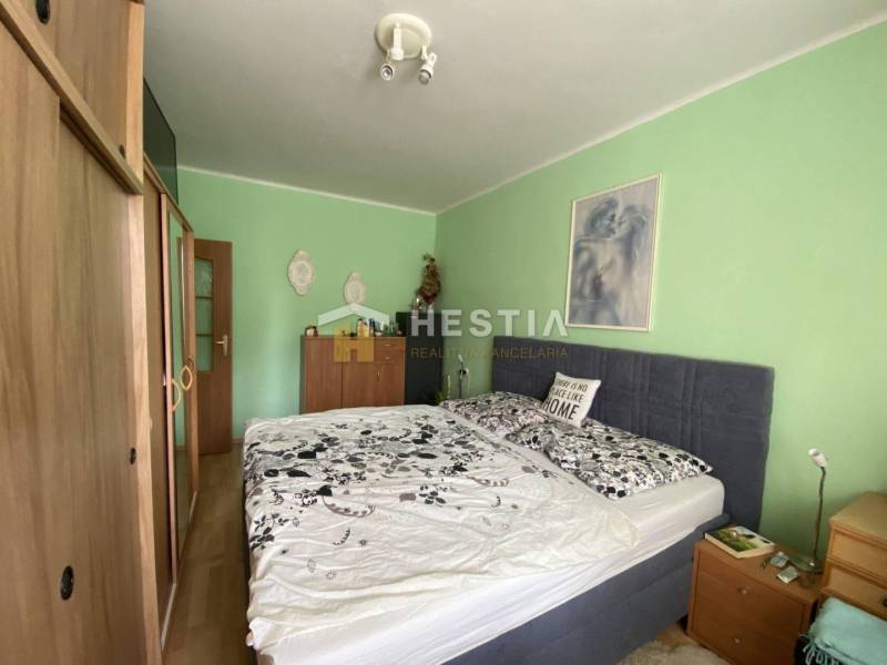 Ložnice v 2pokojovém bytě s postelí a nábytkem, stěny jsou světle zelené.