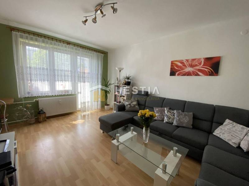 Obývací pokoj s pohodlnou sedačkou, skleněným stolkem a podlahou s dřevěným dekorem v 2-pokojovém bytě.