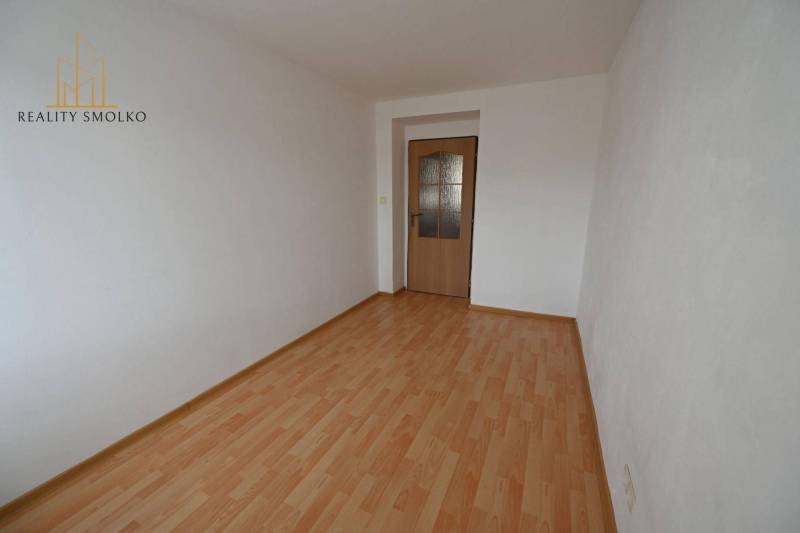 Pokoj v 2-pokojovém bytě s podlahou s dřevěným dekorem a bílými stěnami.