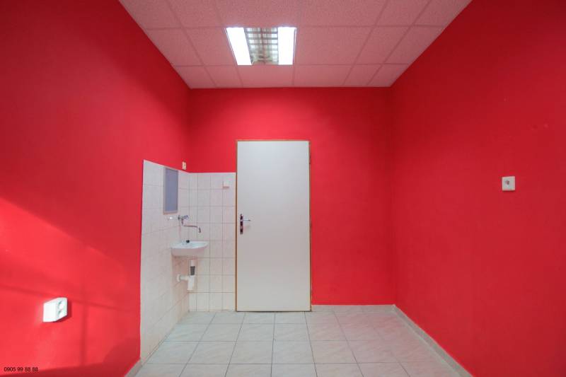 Interiér obchodních prostor, červené stěny, bílé dveře a umyvadlo, keramická dlažba.