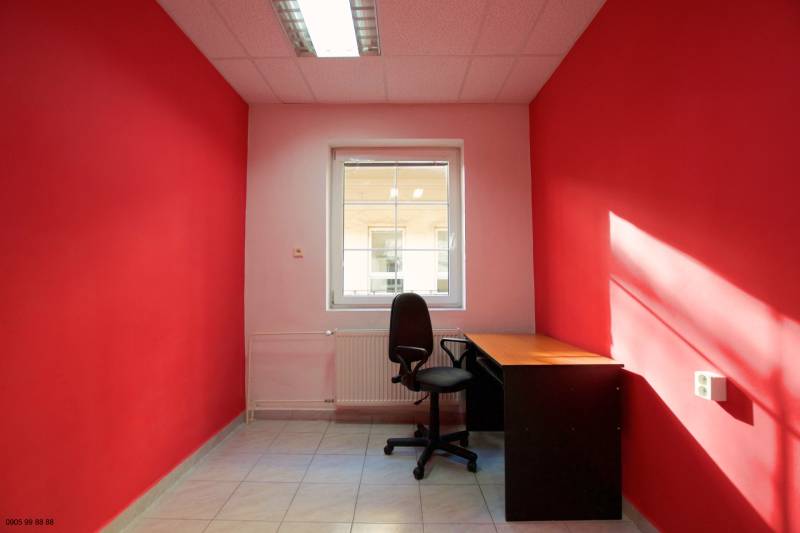 Kancelář s červenými stěnami, černou židlí a stolem, světlý interiér.