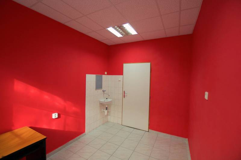 Interiér obchodního prostoru s červenými stěnami, umyvadlem a bílými dlaždicemi.