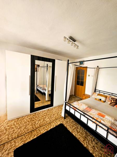 Ložnice v rodinném domě s postelí, kobercem a skříní se zrcadlem.