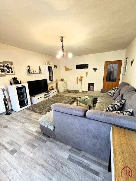 Obývací pokoj v rodinném domě s podlahou s dřevěným dekorem, šedou sedačkou a moderním osvětlením.