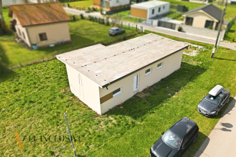 Chata ve Vojce nad Dunajem s rovnou střechou a zaparkovanými auty na travnaté ploše.