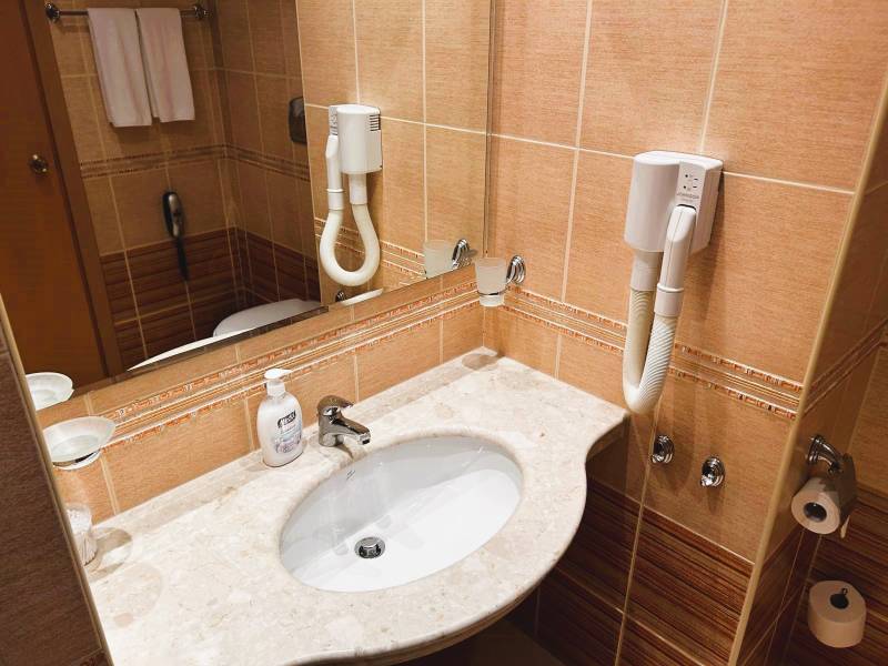 Koupelna v 1-pokojovém bytě s umyvadlem, fénem, mramorovou deskou a zrcadlem.