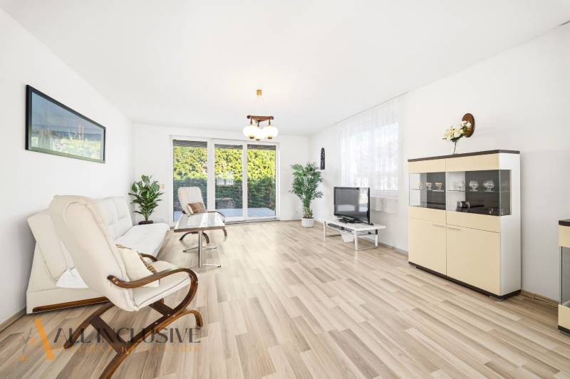 Světlý obývací pokoj s podlahou s dřevěným dekorem, pohovka, křeslo a televize.