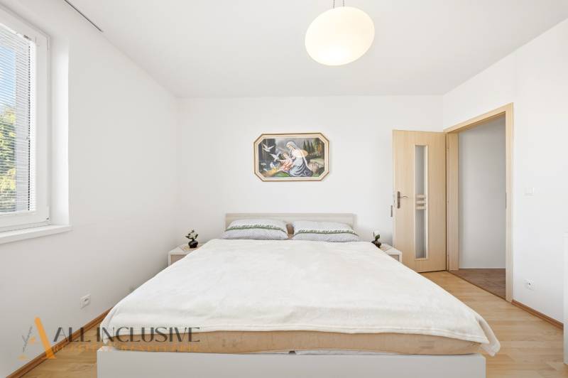 Ložnice v rodinném domě s jednoduchým nábytkem a podlahou s dřevěným dekorem.