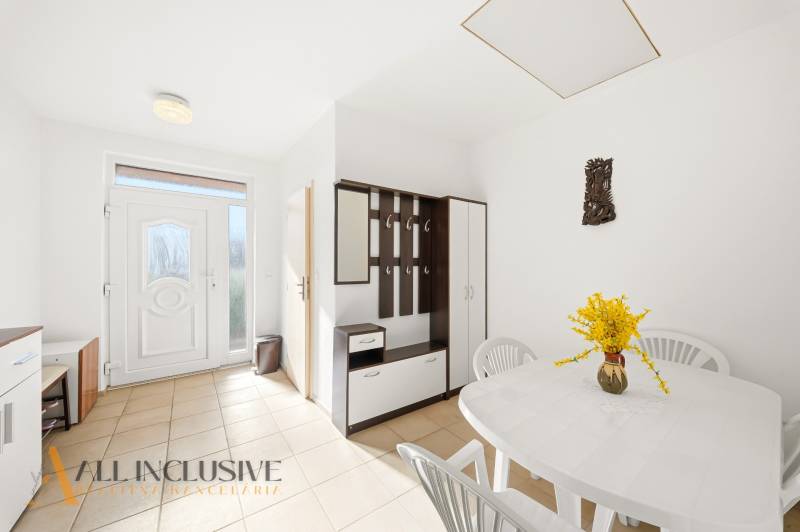 Interiér rodinného domu s bílým stolem, plastovými židlemi a věšákovou stěnou.