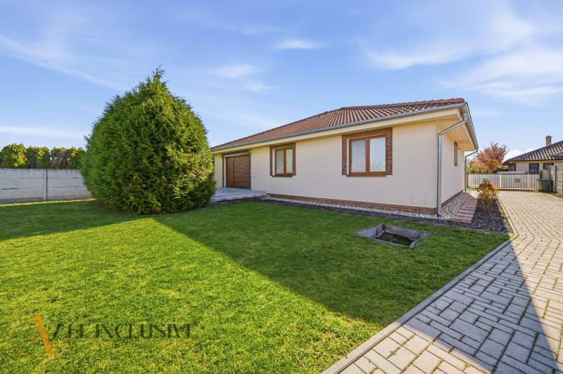 Rodinný dům v Kútnikoch s trávníkem, stromy a dlažbou.