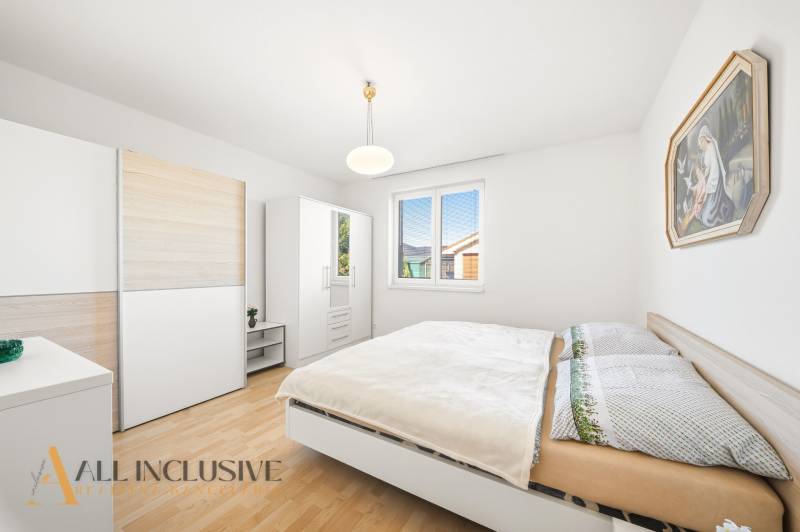 Ložnice v rodinném domě s podlahou s dřevěným dekorem, bílým nábytkem a obrazem.