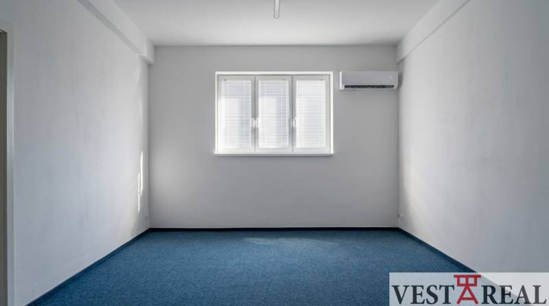 Kanceláře s modrým kobercem, bílými stěnami a klimatizací.