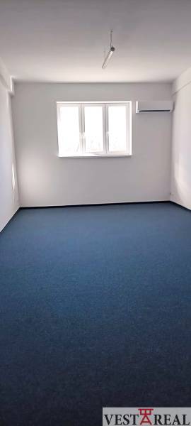 Kanceláře s modrým kobercem a oknem, umístěné na Chovateľské ulici v Trnavě.