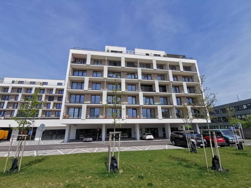 Bytový dům na ulici Eduarda Wenzla s parkováním a garážemi v popředí.