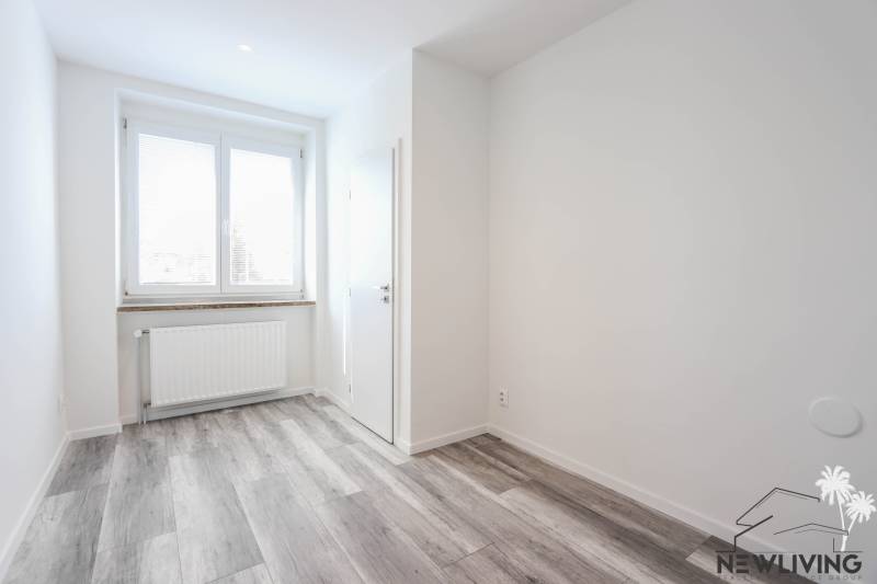 Světlý pokoj s podlahou s dřevěným dekorem a oknem v 3-pokojovém bytě.