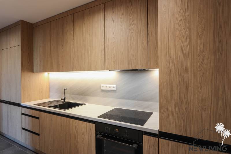 Kuchyně v 3-pokojovém bytě s dřevěným dekorem kuchyňské linky a zabudovanými spotřebiči.