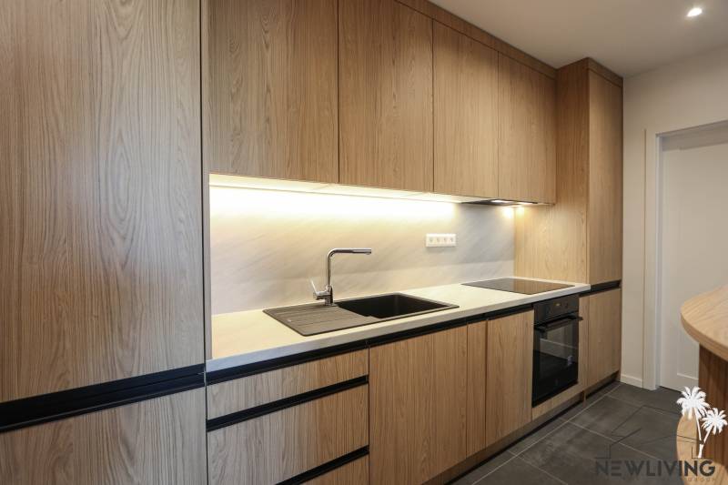 Kuchyně s dřevěným dekorem, černými detaily, vestavěnými spotřebiči ve 3-pokojovém bytě.