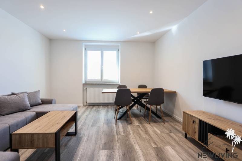 Obývací pokoj s podlahou s dřevěným dekorem, sedačkou, jídelním stolem a televizí ve 3-pokojovém bytě.