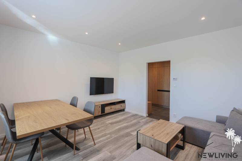 Obývací pokoj v 3-pokojovém bytě s podlahou s dřevěným dekorem a dřevěným nábytkem.