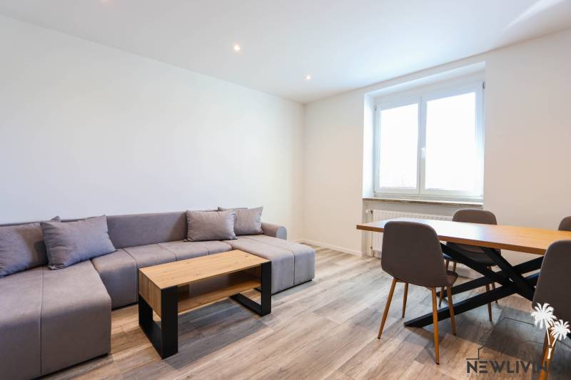 Obývací pokoj s rohovou sedačkou, jídelním stolem a podlahou s dřevěným dekorem.