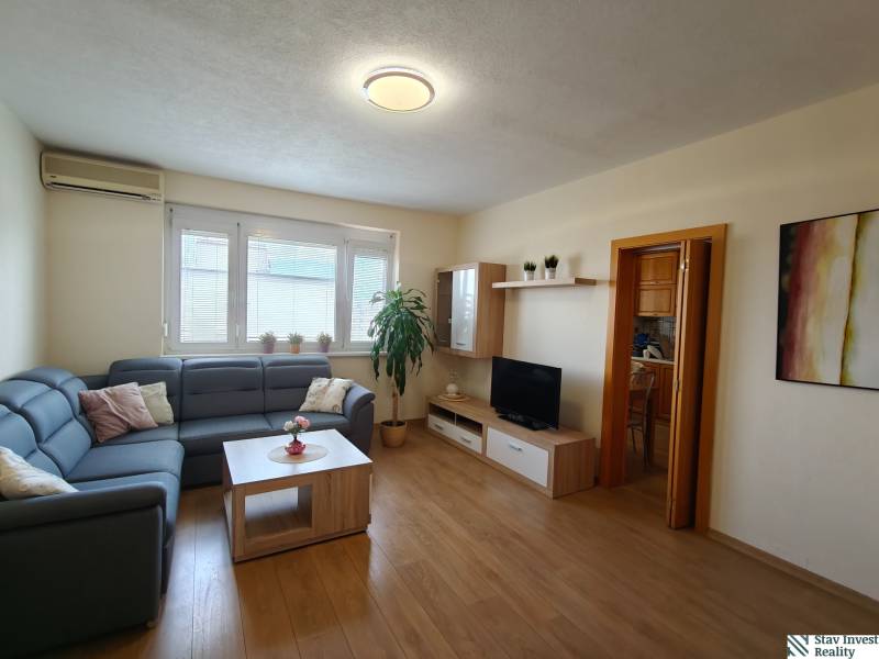 Světlý obývací pokoj s modrou sedačkou v 3-pokojovém bytě, podlaha s dřevěným dekorem.