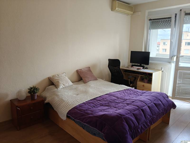 Ložnice v 3-pokojovém bytě s postelí, pracovním koutem a podlahou s dřevěným dekorem.