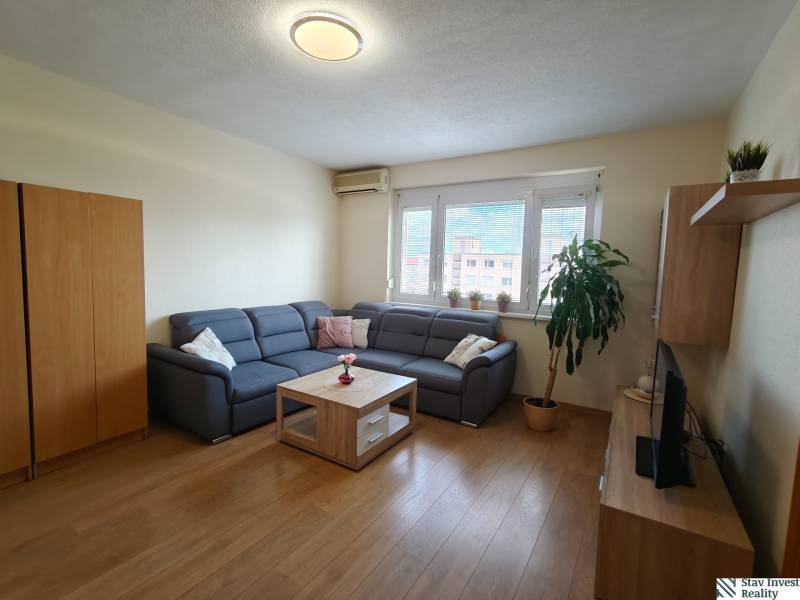 Obývací pokoj s rohovou sedačkou, podlahou s dřevěným dekorem a TV ve 3-pokojovém bytě.