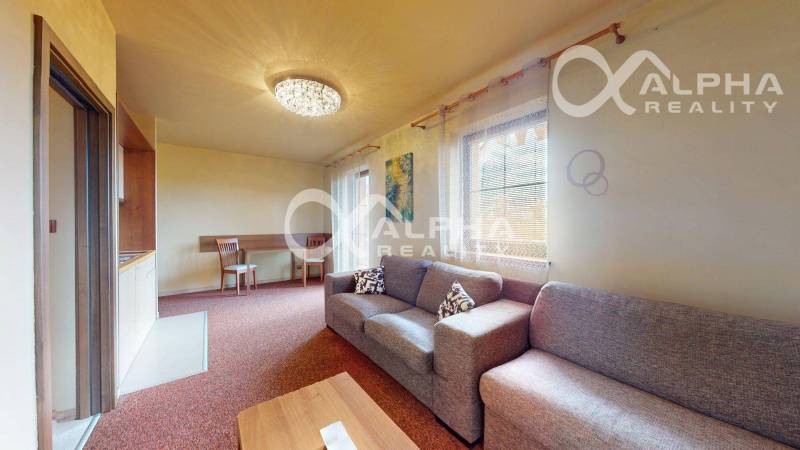 Obývací pokoj v 2pokojovém bytě s pohovkou, jídelním stolem a závěsy.