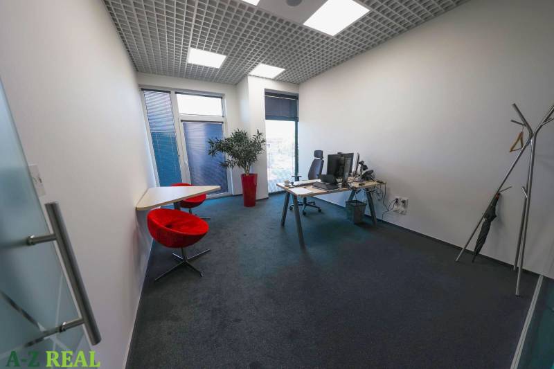 Interiér kanceláře s počítačovým stolem, červenými židlemi a dekorativní rostlinou.