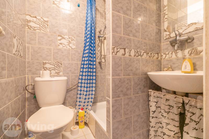 Koupelna v 1-pokojovém bytě s umyvadlem, toaletou a sprchovým koutem s modrým závěsem.