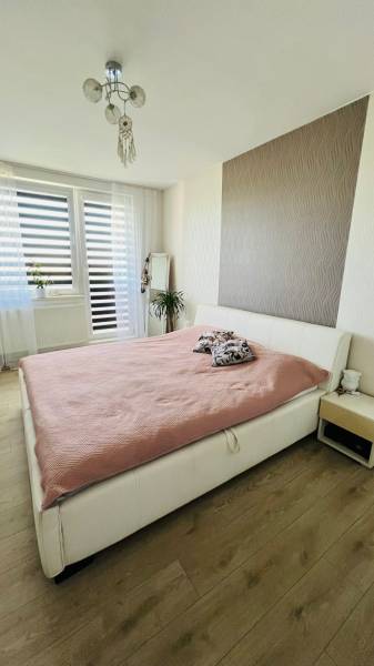 Světlá ložnice s velkou postelí, zrcadlem a podlahou s dřevěným dekorem ve 3-pokojovém bytě.