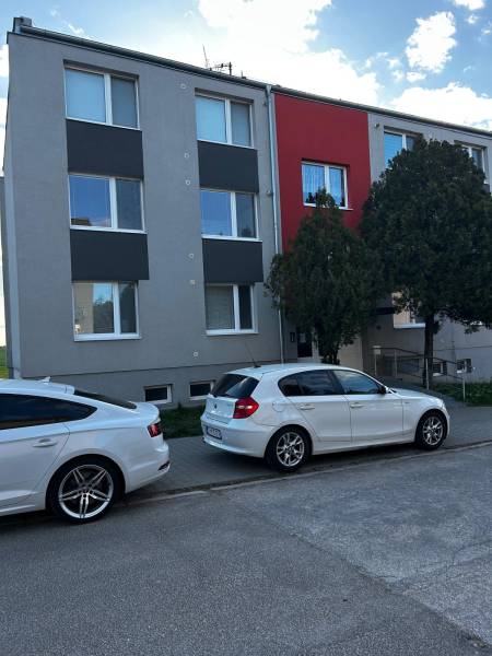 Bytový dům v Gbelech s moderní fasádou a zaparkovanými auty před 3pokojovým bytem.