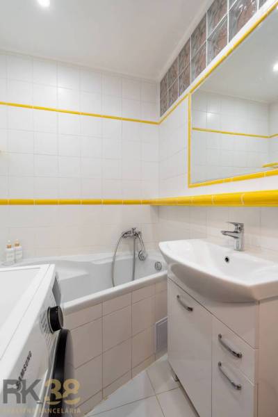 Koupelna rekreačního apartmánu s vanou, umyvadlem, pračkou a bílými obklady.