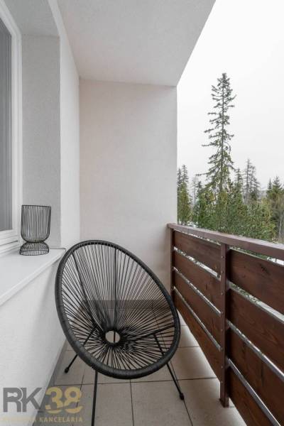 Balkon rekreačního apartmánu v Popradu s černým křeslem a výhledem na stromy.