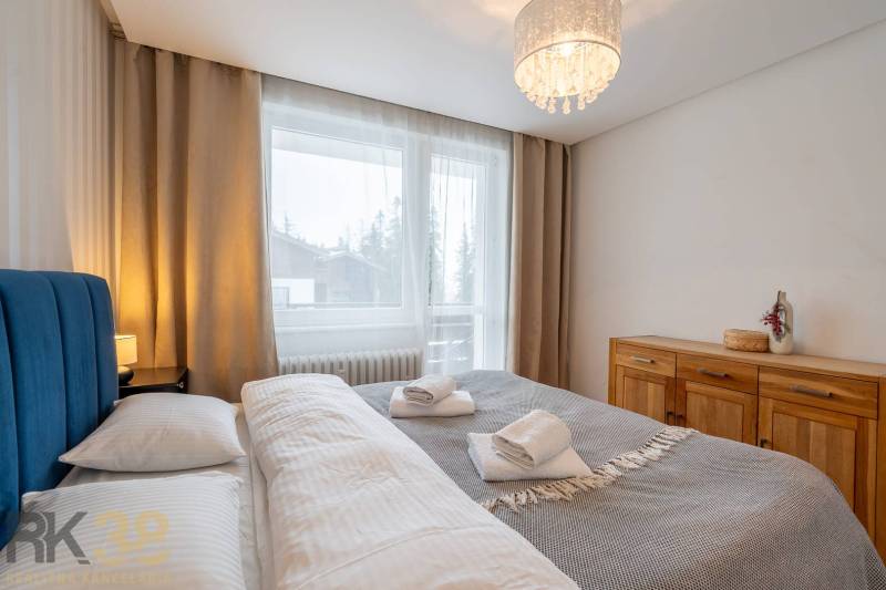 Ložnice v rekreačním apartmánu s manželskou postelí a komodou, okno s výhledem.