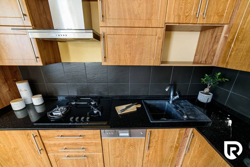 Kuchyňská linka v 2-pokojovém bytě, s podlahou s dřevěným dekorem a tmavými obklady.