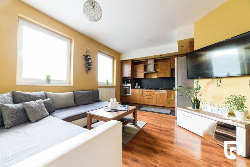 Obývací pokoj v 2-pokojovém bytě s kuchyňským koutem a podlahou s dřevěným dekorem.