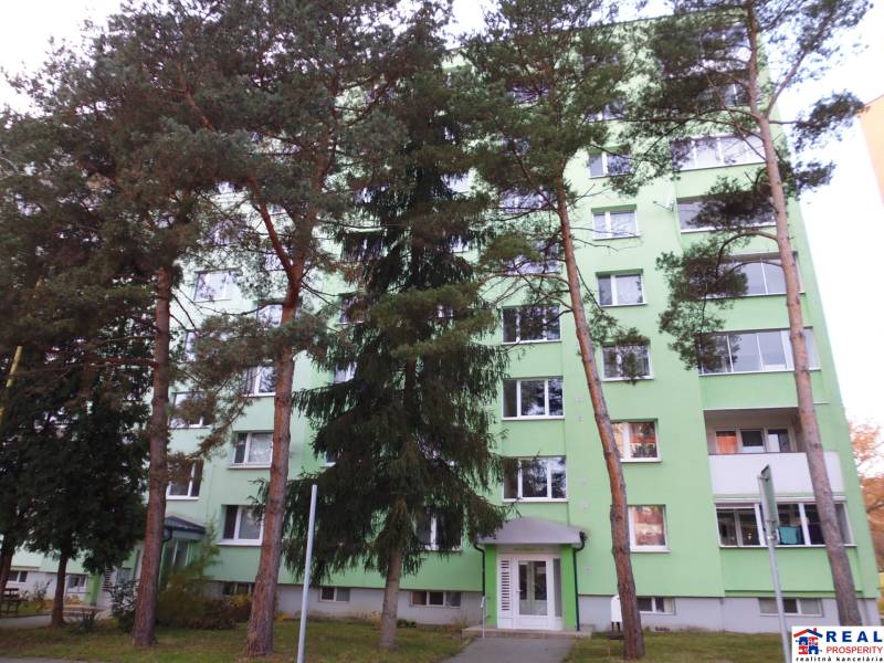 Zelená fasáda bytového domu obklopená stromy ve městě Prešov nabízí 2pokojový byt.