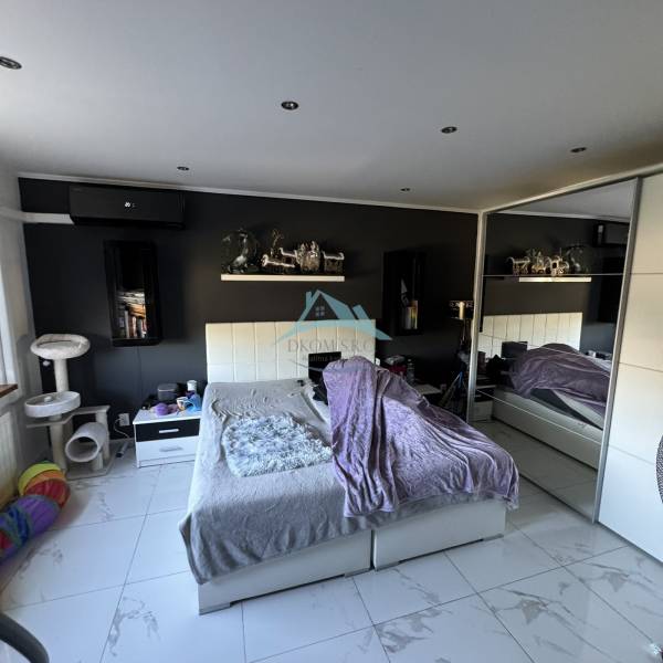 Ložnice v dvoupokojovém bytě s bílým nábytkem, dekoracemi a kočičími doplňky.