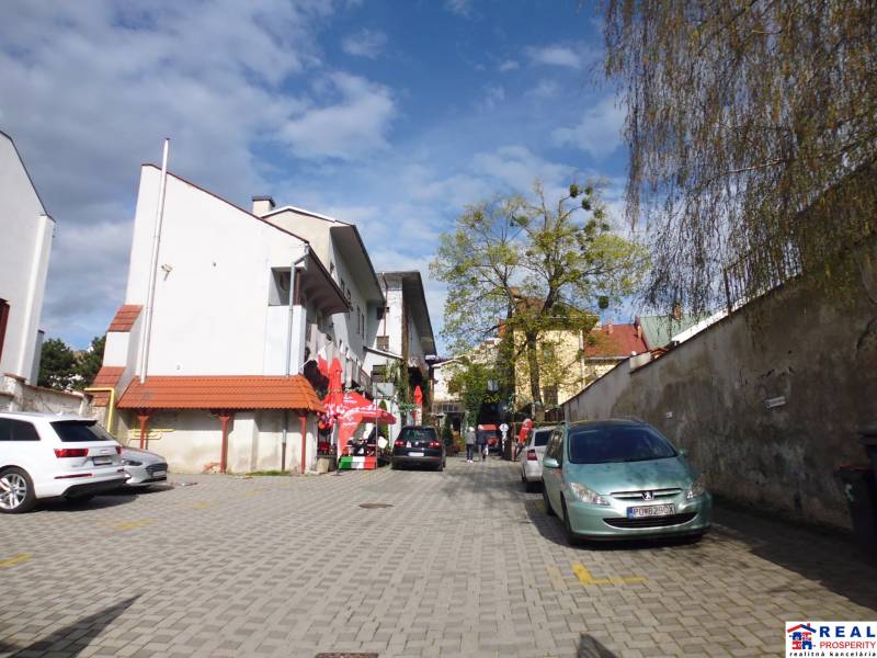 V Prešově na Hlavní ulici jsou zaparkovaná auta a chodci na dlážděné ploše.