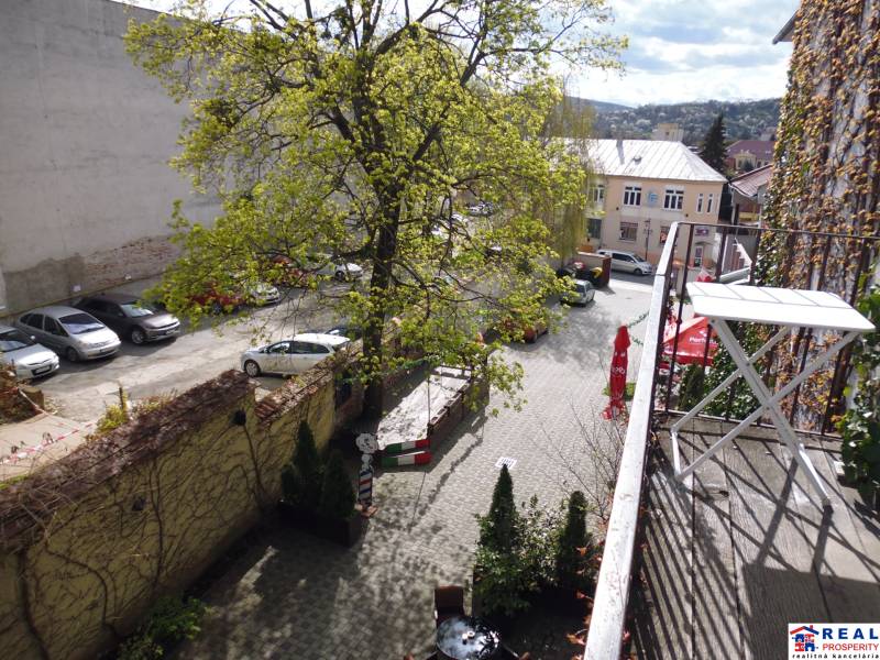 Pohled z balkonu 3-pokojového bytu na Hlavní ulici v Prešově s parkovištěm a zelení.