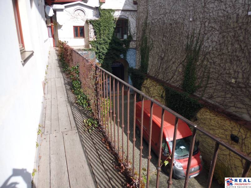 Úzký balkon s dřevěným dekorem nad dvorem a červenou dodávkou, Hlavní ulice, Prešov.