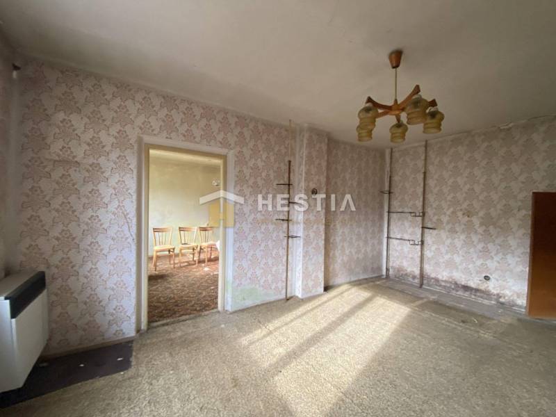 Pokoj v rodinném domě s květinovými tapetami, kobercovou podlahou a lustrem.