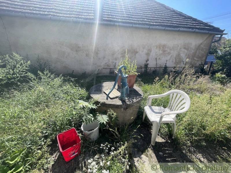 Zahrada v Jatove s pumpou, plastovou židlí a kbelíkem u rodinného domu.