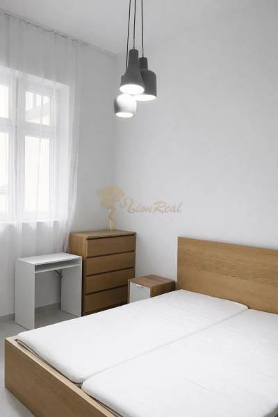 Ložnice s dřevěným nábytkem a závěsným osvětlením v dvoupokojovém bytě.