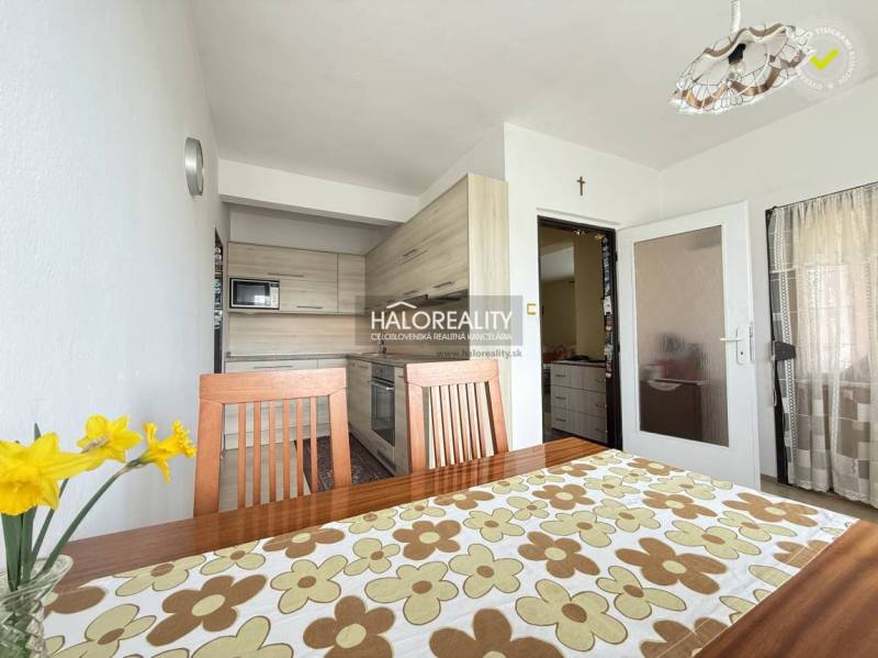 Jasná kuchyně v rodinném domě s dřevěným nábytkem a dekorativním stolním ubrusem.