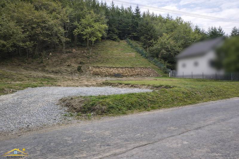 Svažitý pozemek v obci Makov s příjezdovou cestou a okolním lesním porostem. Pozemky - bydlení.