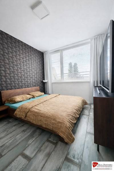 Ložnice v 2-pokojovém bytě s geometrickou tapetou a podlahou s dřevěným dekorem.